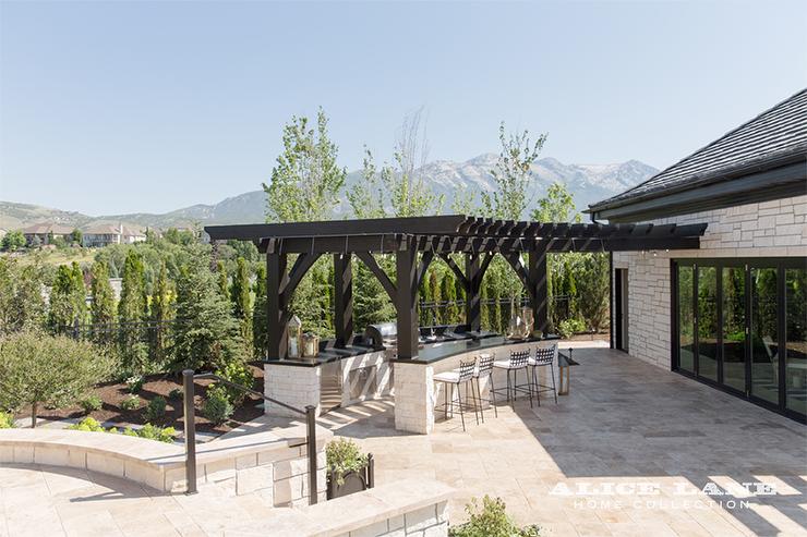 Cuisine design de terrasse abritée par une grande pergola en bois. Chaises en fer forgé pour le coin bar. Plutôt réussi cet aménagement d'une cuisine d'été avec bar dans le jardin.