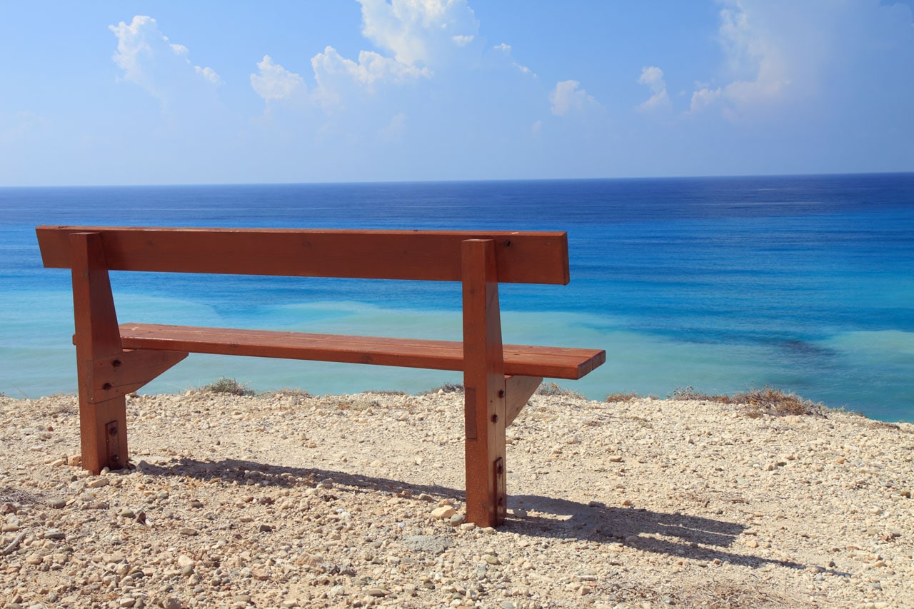 Banc de jardin tendance avec deux planches en bois ainsi que deux pieds. Parterre en gravillons et graviers, panorama sur une magnifique mer avec plusieurs nuances bleues. crédit photo©Public Domain Pictures