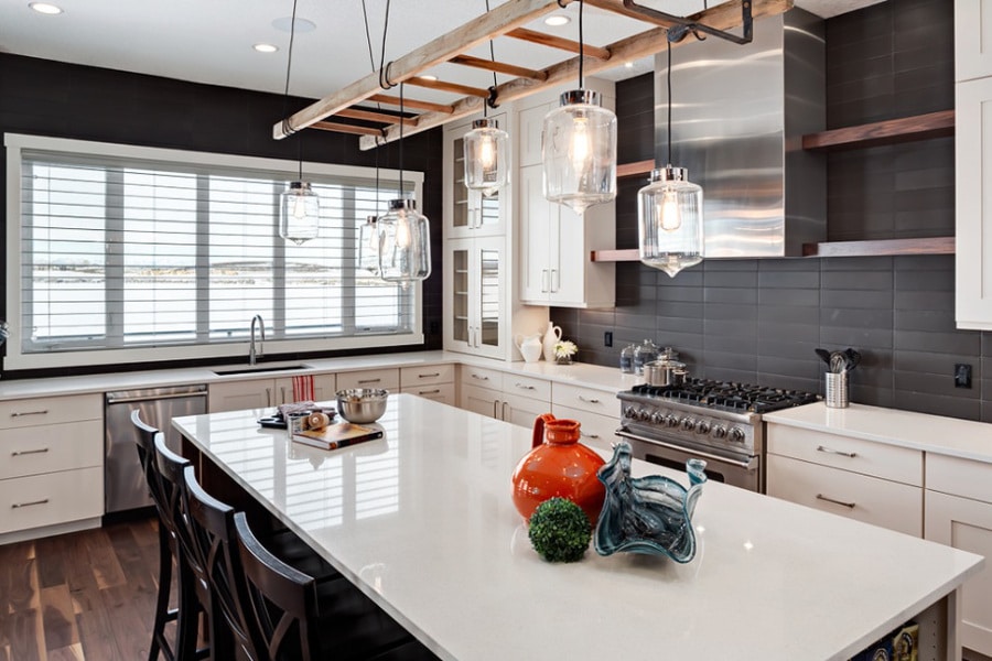 Décoration pour donner à votre cuisine un air de campagne avec lampes rustiques suspendues à une échelle en bois. Parquet, table blanche rectangulaire avec différentes chaises. Source : https://www.tricklecreekhomes.ca/
