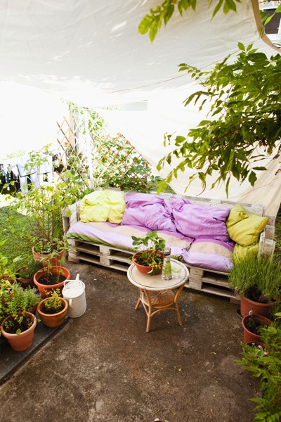 Canapé d’extérieur en palette, trois places assise et dossier gros cousins parme et citron, guéridon en table basse, pots de fleurs. Environnement green power. canape-dangle-en-palettes-de-bois-steiner-wolfgang-3