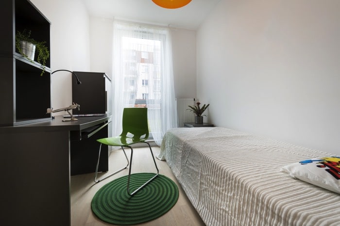 Chambre d'ado garçon de forme rectangulaire avec bureau anthracite à gauche, chaise verte claire sur tapis rond en spirales. Lit blanc une place, fenêtre avec rideau transparent. deco-chambre-ado-garcon-cinematographer-901
