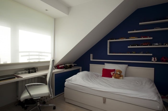 Chambre d'ado garçon originale décorée avec des couleurs blanches et bleue claire. Lit deux places avec petite peluche, étagères avec petites voitures de collection dessus. deco-chambre-ado-garcon-copyright-basileus