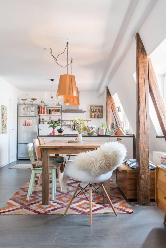 Salle à manger boho-chic moderne blanche et grise. Tapis style africain en losanges de différentes couleurs en-dessous d'une table en bois dans une pièce blanche.