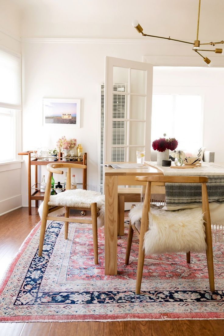 Salle à manger boho-chic en bois hêtre dans une pièce toute blanche avec un luminaire minimaliste à la forme originale. Grand tapis rectangulaire au style africain en-dessous de la table.