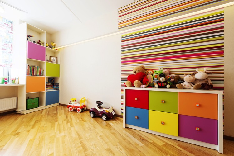Meubles bibus et nombreux cubes de rangement colorés, chambre d'enfant gaie et pratique. Panneau mural lignes de couleurs chatoyantes, grand espace libre au sol, plancher bois clair.