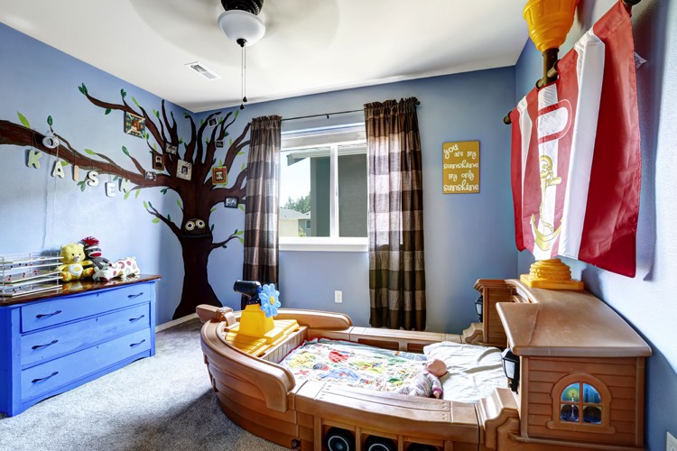 Chambre garçon originale très décorée, couleur bleu ciel et chocolat, arbre en stickers sur angle de mur. Lit en forme de navire au centre de la pièce, commode bleu 3 tiroirs.