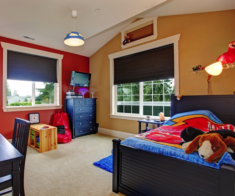 2 grandes fenêtres pour éclairer cette chambre d'enfant, couleurs dominantes : bleu, brique, ocre et noirs. Lit au centre, un bureau et sa chaise en bois peint en noir font face, commode disposée en angle entre les fenêtres, cube au sol sert de séparation de la pièce en 3 zones.