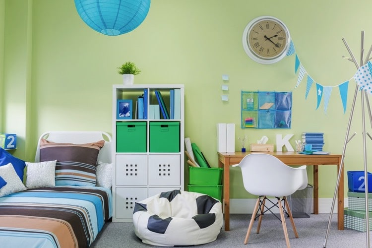 Chambre pastel, boule chinoise bleue en luminaire. Grosse horloge au mur et fanion en déco, lit placé sous la fenêtre, mobilier disposé en enfilade sur le même coté, meuble à casier blanc et bureau en bois. Pour assise un pouf ballon de foot et une chaise blanche pour le bureau.