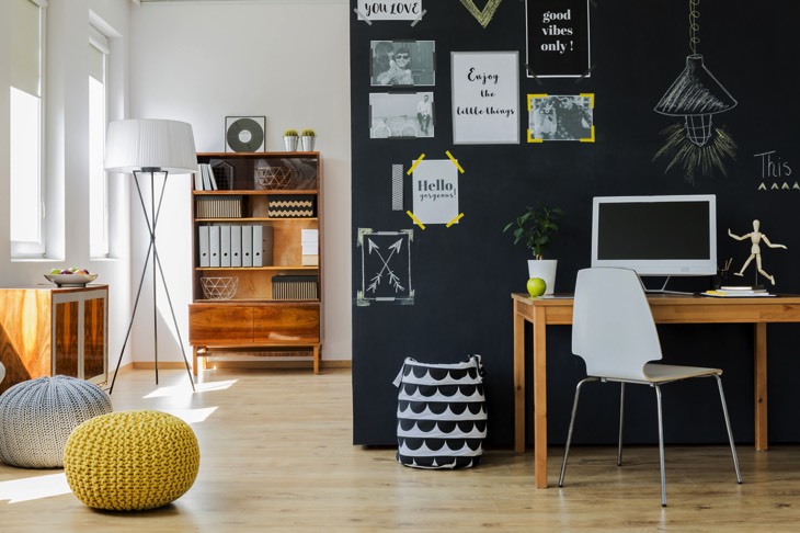 Bureau design ergonome en bois pour adolescents. Pièce design moderne avec une étagère en bois, deux poufs, du parquet, un mur original avec inscriptions et dessins dessus sur fond anthracite.
