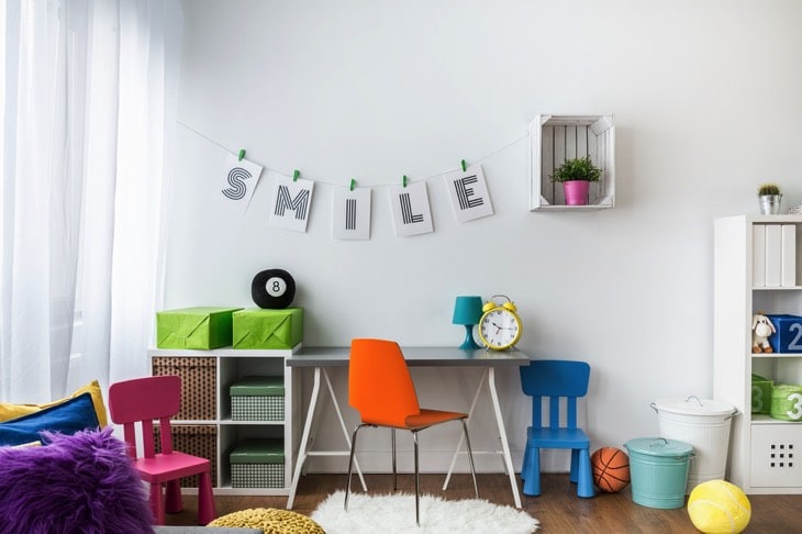 Idée d'un bureau d'ado pop avec une chaise orange, une bleue et une violette, multitude d'objets comme un ballon de basket, une horloge jaune, un tapis blanc et des rangements à droite ainsi que du parquet.