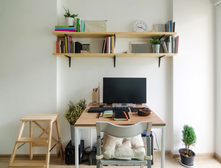 Idée bureau en bois hêtre minimaliste pour adolescents avec PC et clavier, des étagères en hauteur, livres et accessoires dessus. Parquet et mur blanc.