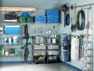 Garage aménagé avec différentes rangements disposés en L sur mur bleu clair. VTT, caisses en bleu, échelle classique et divers pinceaux.