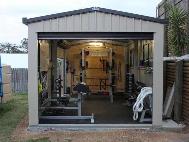 Petit garage aménagé relooké en véritable salle de musculation avec poids et différentes machines. Fenêtres et look industriel avec carrelage gris anthracite.