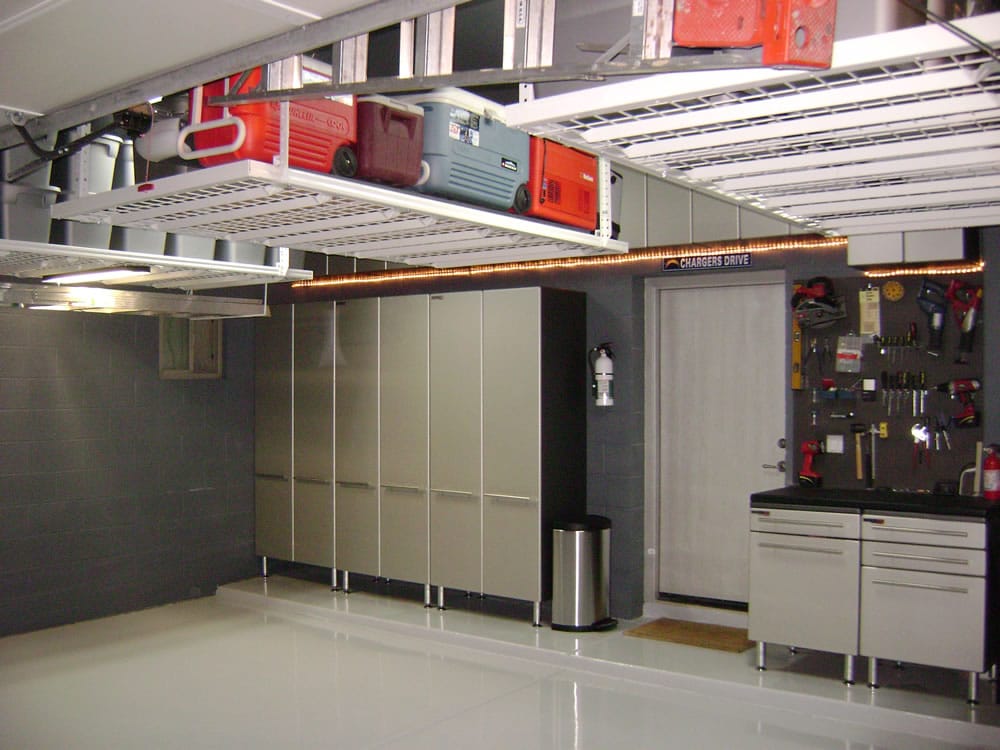 Garage aménagé avec rangements coulissants blancs en hauteur. Grands casiers et petit étable avec tiroirs et crochets pour mettre différents outils.