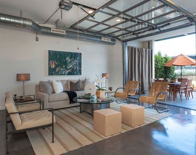 Garage aménagé au style industriel avec look moderne et mur blanc. Salon composé d'un fauteuil, de sièges et de poufs avec une table en verre ronde au milieu.