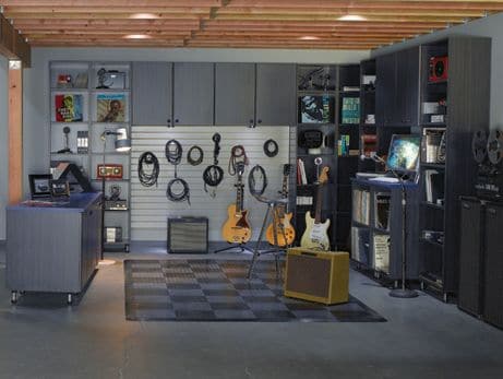 Garage aménagé en salle de musique avec mur principalement en gris. Sono, guitares, basse, enceintes, micro et divers matériaux d’enregistrement.