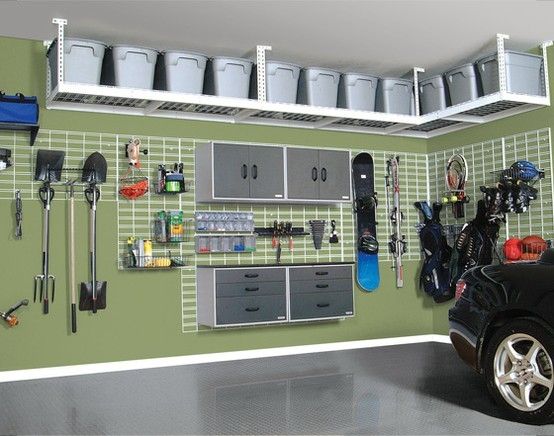 Garage aménagé en vert clair avec sol gris et étagères blanches accrochés au plafond. Rangements avec tiroirs, pelles, snowboard et sacs.