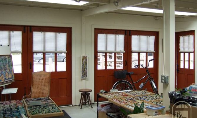 Garage aménagé blanc avec différentes portes rouges avec carreaux en verre. Multitude de différentes épices sur des tables avec peinture sur la gauche.