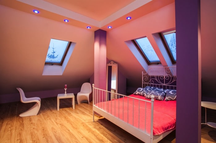 Déco sympa et ludique pour une chambre d’ado fille avec des couleurs oranges. Spots lumineux bleus au plafond, lit deux places rose, poteaux violets, petite table blanche avec deux chaises, parquet. chambre-ado-fille-photographee-eu-012