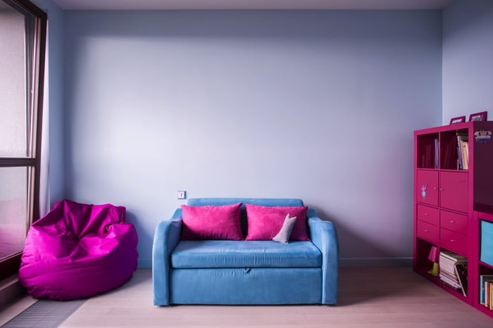 Déco sympa rose fushia, violette et bleue claire pour une chambre d’ado fille. Pièce avec mur gris-bleu, canapé deux places, rangements avec tiroirs à droite et pouf à gauche. chambre-ado-fille-photographee-eu-03892
