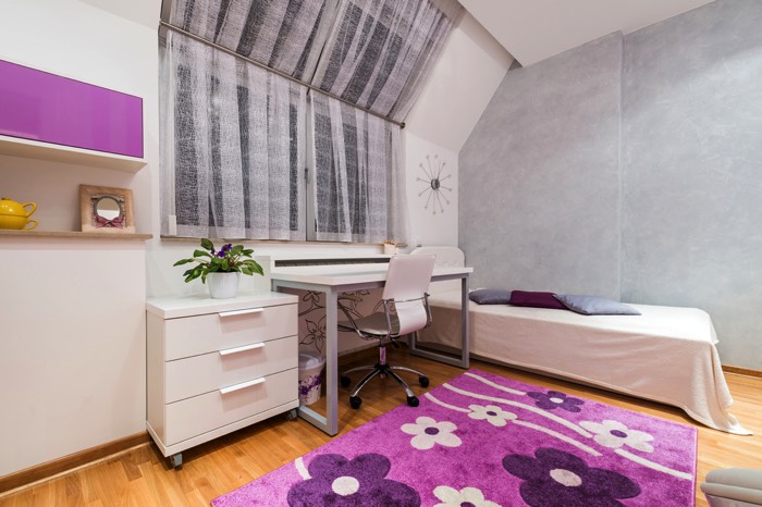 Décoration blanche, grise et violette claire pour une chambre d’ado fille. Lit une place, table avec chaises à roulettes, rangement avec trois tiroirs, parquet et tapis. chambre-ado-fille-shutterstock_249886066