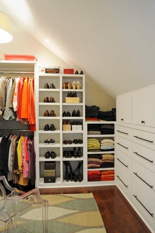 Dressing dans combles tout en blanc avec parquet stratifié et tapis vert-blanc-jaune. Étagère servant pour ranger de multiples chaussures, bottes et talons.