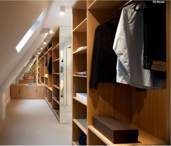 Dressing dans des combles avec plafond blanc, fenêtre rectangulaire, miroir au fond et moquette beige. Rangements en étagères en bois chêne.
