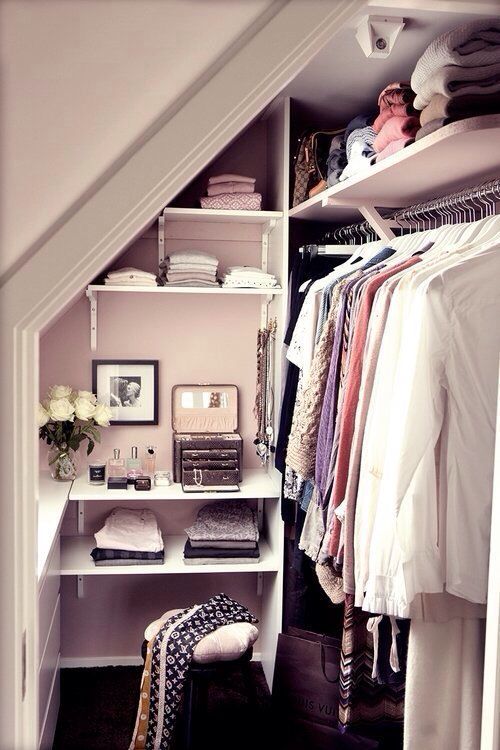 Dressing dans des combles en blanc avec étagères contenant des draps, couvertures, parfums et fleurs blanches dessus. Cravates sur chaise en bois avec coussin blanc.