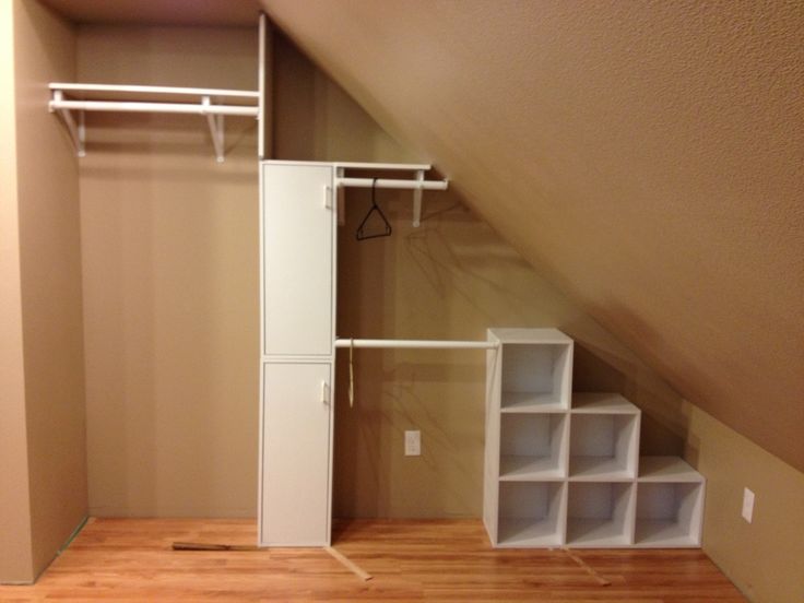Dressing dans des combles totalement vide avec plafond marron et parquet stratifié. Rangements avec petites cases carrés blanches.