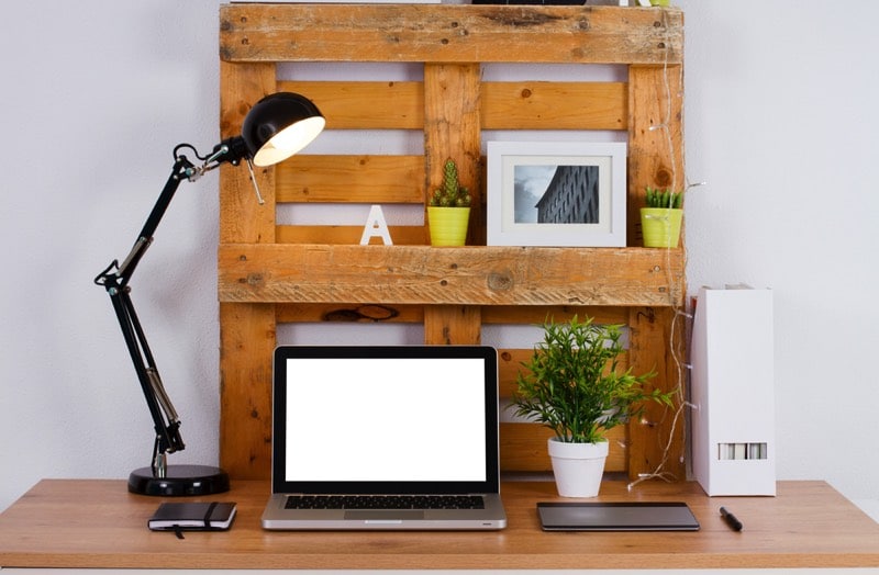 Bureau en palettes à trois niveaux avec cadre photo blanc et deux petits pots jaunes contenant des cactus. Ordinateur portable moderne, lampe noire et petit carnet. fabriquer-bureau-en-palette-de-bois-copyright-gines-romero-2