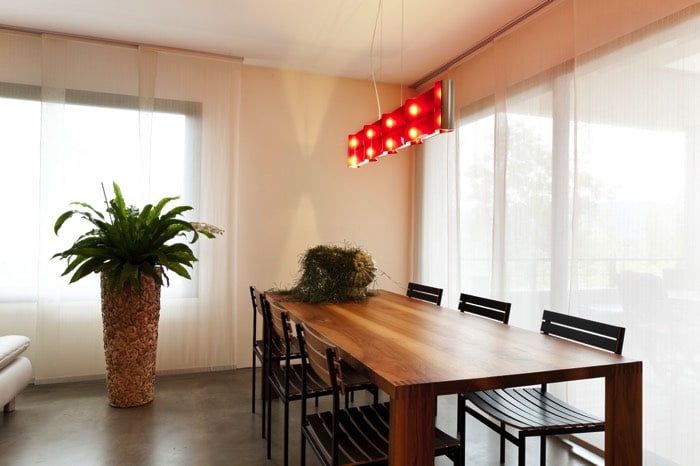 Table salle à manger en bois (chêne) dans un style green power. Lampe originale suspendue en rouge dans une pièce lumineuse.
