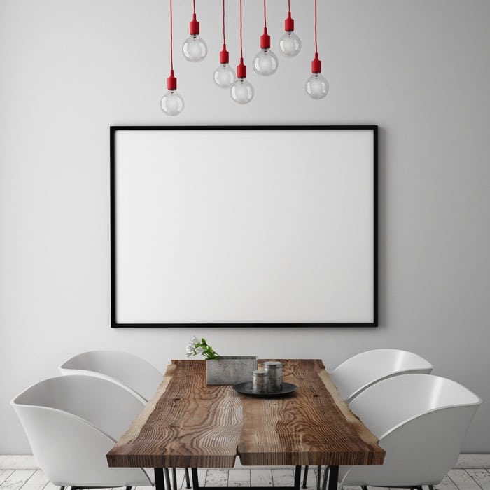 Table de salle à manger en vieux bois avec quatre fauteuils. Pièce toute blanche avec lampes suspendues rouges.