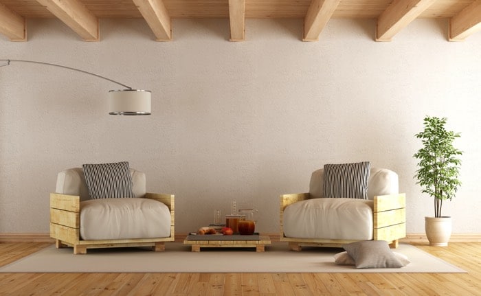 Fauteuil en palette blanc et gris sur tapis rectangulaire et parquet. Petite table basse, plantes à droite, lampe à droite et plafond en bois.
