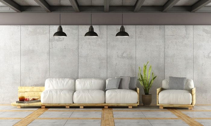 Fauteuil en palette blanc avec des coussins gris et une plante entre. Trois lampes suspendues noires, mur gris et parquet mixé avec du carrelage.