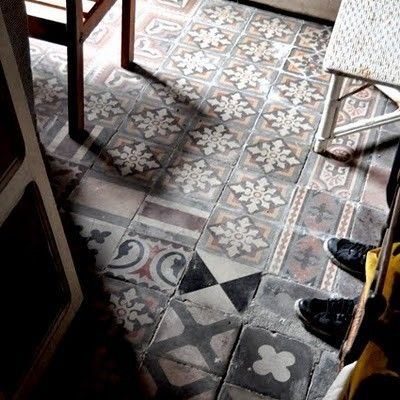 Carreaux à divers motifs avec couleurs dont le gris ainsi que le noir. Pièce avec table basse blanche à droite et table rectangulaire en bois à gauche.