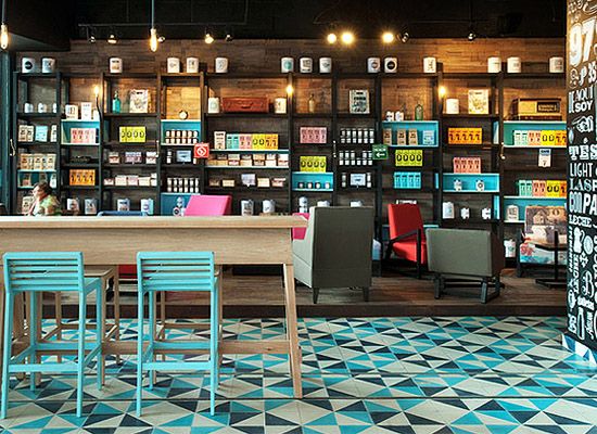 Carreaux de ciment style pop moderne avec des couleurs dont le bleu et le blanc. Bar en bois, différents fauteuils rouges, roses, gris et diverses étagères.