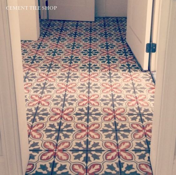 Carreaux de ciment de deux formes, dont une semblable à une fleur, avec couleurs rouge et bleue. Pièce avec différentes portes blanches.