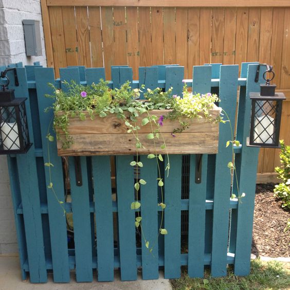 Jardinière en palette en bleu clair avec différentes plantes et fleurs dedans. Deux belles lanternes grises avec deux bougies blanches dedans.