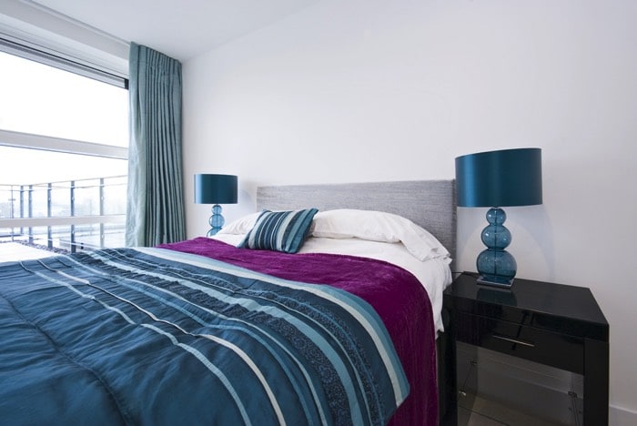 Couleur bleue dominante dans cette chambre avec mur en blanc et table de chevet noire. Décoration moderne et tendance avec baie vitrée donnant sur une terrasse. couleur de chambre : bleu