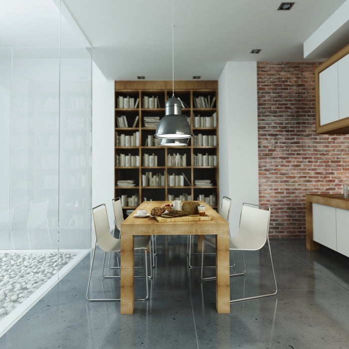 Briques rouges dans une salle à manger avec paroi en verre sur le côté et galets en extérieur. Spots lumineux au plafond blanc et bibliothèque en bois en fond.