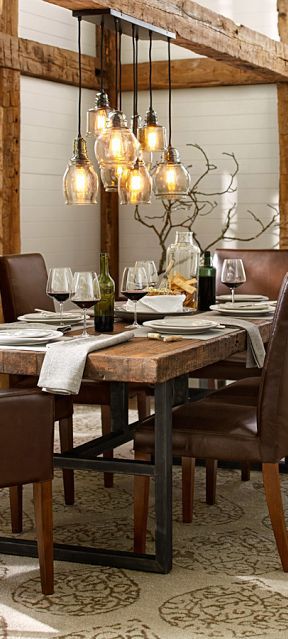 Salle à manger au style campagnard avec table rectangulaire en bois et sièges en cuir marron sur tapis beige. Lampes en verre suspendues à une poutre.