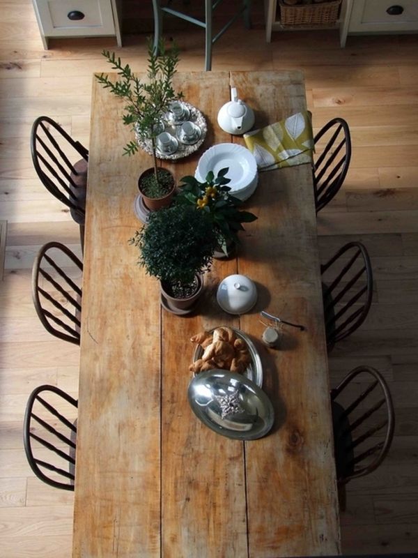 Salle à manger campagnarde avec parquet et table rectangulaire en bois avec chaises noires. Plantes en pot, vaisselle blanche et tasses de thé en porcelaine.