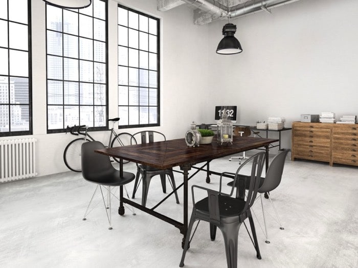 Salle à manger style industriel avec table rectangulaire en bois wengé, différents accessoires dessus, et différentes chaises noires sur sol blanc-gris. Trois fenêtres quadrillés en verre et lampe noire suspendue.