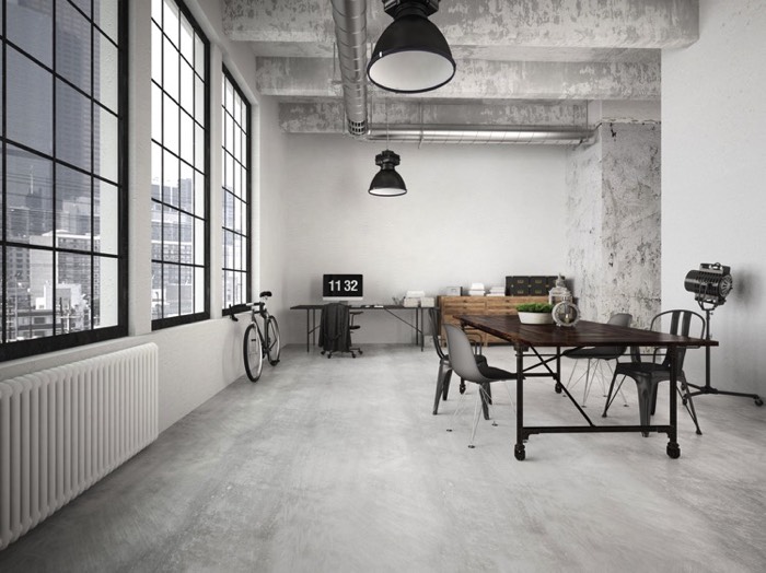 Salle à manger style industriel avec table sur roulettes à droite et espace bureau/plan de travail en fond. Vélo contre mur, vue sur la ville et les buildings.