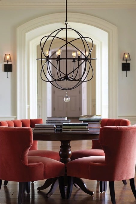 Moderniser une salle à manger traditionnelle avec table ronde en bois wengé et lumière originale moderne suspendue. Quatre fauteuils orange prononcé et parquet.