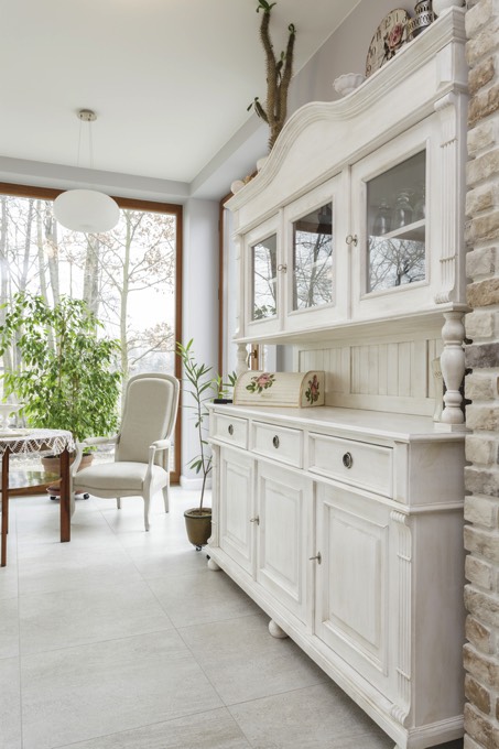 Idée déco pour moderniser une salle à manger traditionnelle toute blanche avec table en bois, plantes et baie vitrée. Meuble blanc doté de trois tiroirs et rangements en-dessous.
