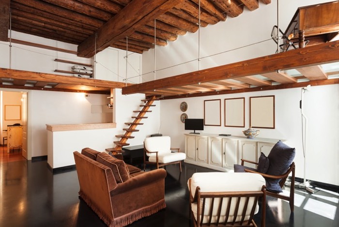 Salle à manger traditionnelle blanche et en bois avec salon composé d'un fauteuil marron, de chaises et de coussins en bleu. Style chalet avec escalier et bureau en haut.