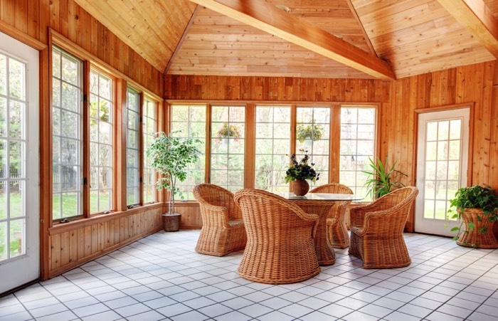 Salle à manger traditionnelle modernisée avec quatre sièges tressés et table en verre. Carrelage blanc classique, différentes fenêtres blanches avec vue sur jardin et petites plantes.