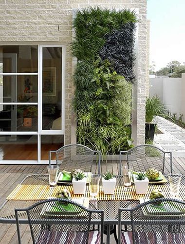 Mur végétal de balcon sur mur en briques de pierres beiges. Baie vitrée en verre et table en verre rectangulaire en aluminium sur parquet.