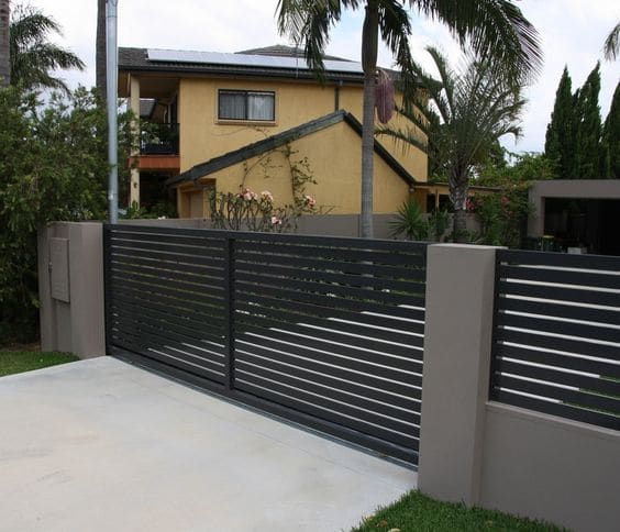 Portail aluminium contemporain couleur gris foncé style moderne avec barreaux horizontaux. Multitude de palmiers et allée bétonnée.